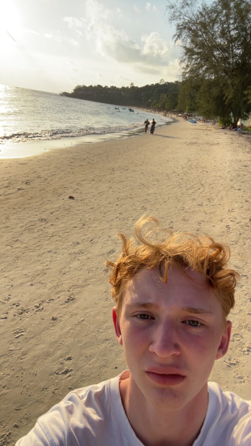 Felix Tinnerholm on an empty beach at golden hour, longtail boats offshore
